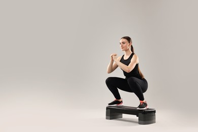 Photo of Young woman doing aerobic exercise with step platform on light background. Space for text