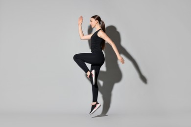 Photo of Young woman doing aerobic exercise on light grey background