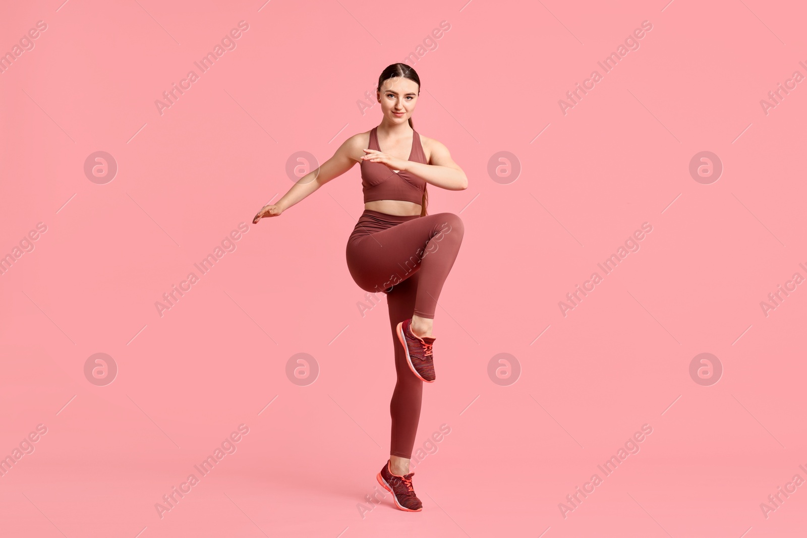 Photo of Young woman doing aerobic exercise on pink background