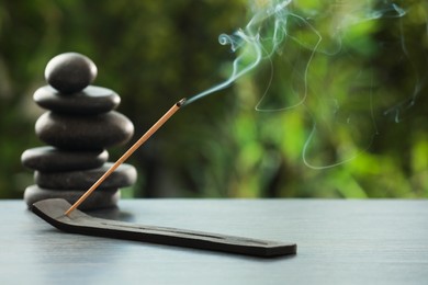 Photo of Incense stick smoldering in holder and spa stones on wooden table outdoors, space for text. Om ligature