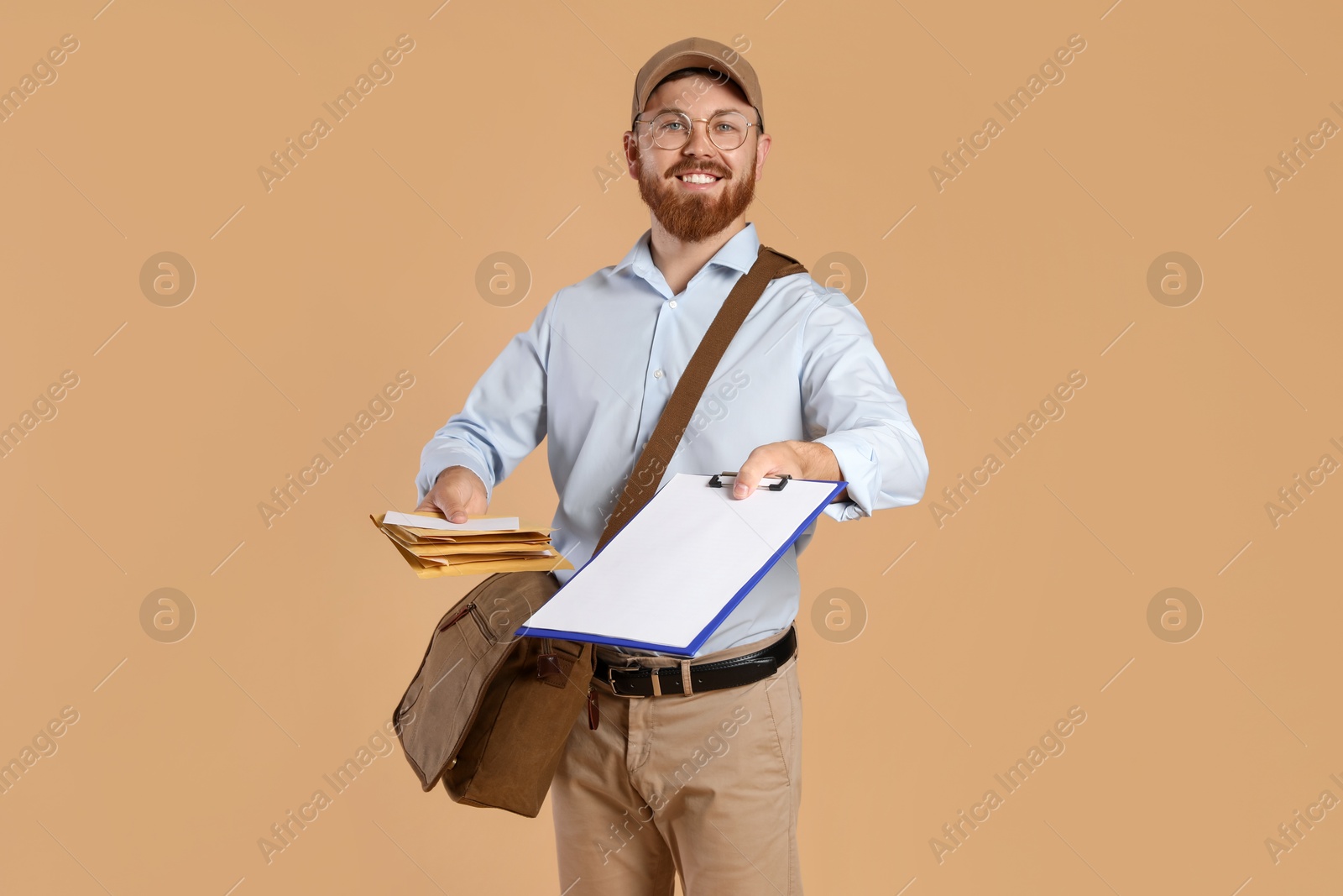 Photo of Happy young postman with leather bag delivering letters on brown background