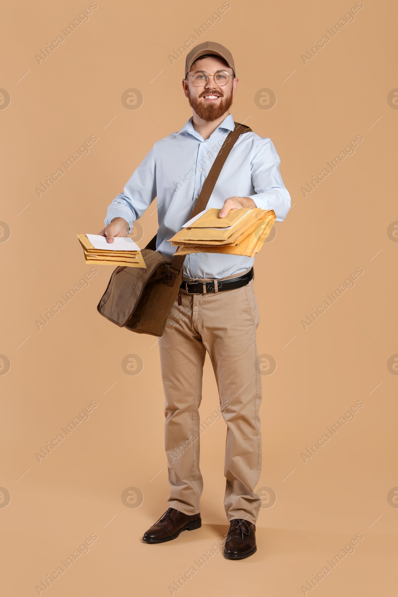 Photo of Happy young postman with leather bag delivering letters on brown background