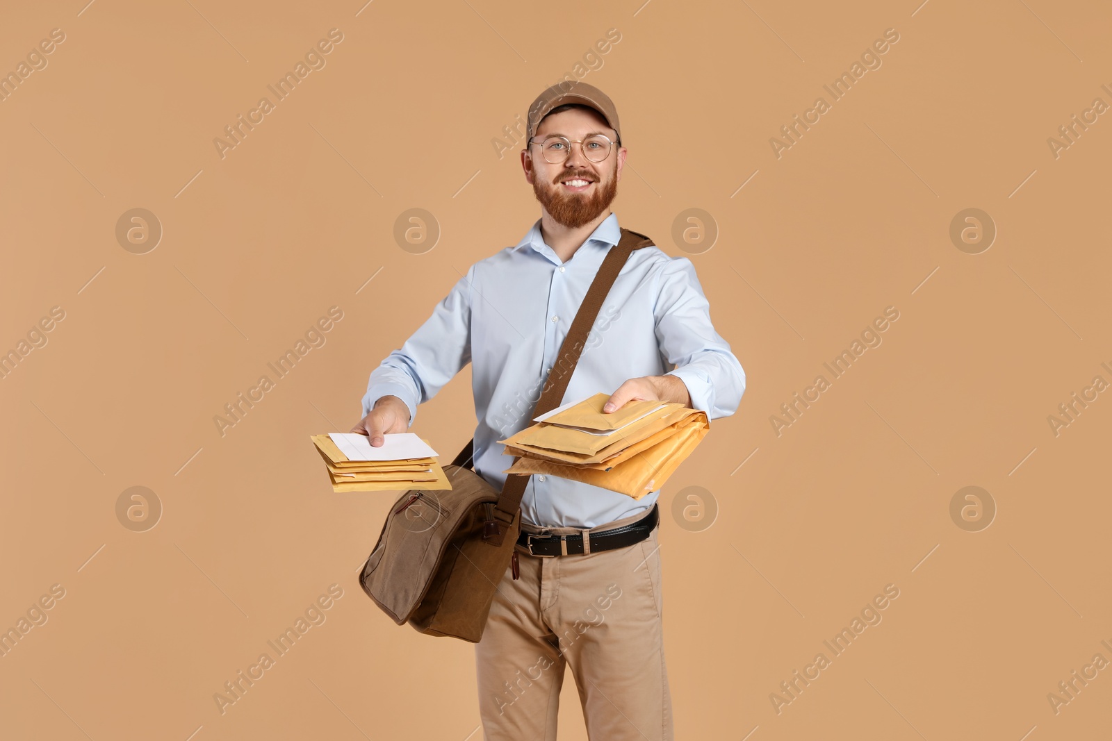 Photo of Happy young postman with leather bag delivering letters on brown background