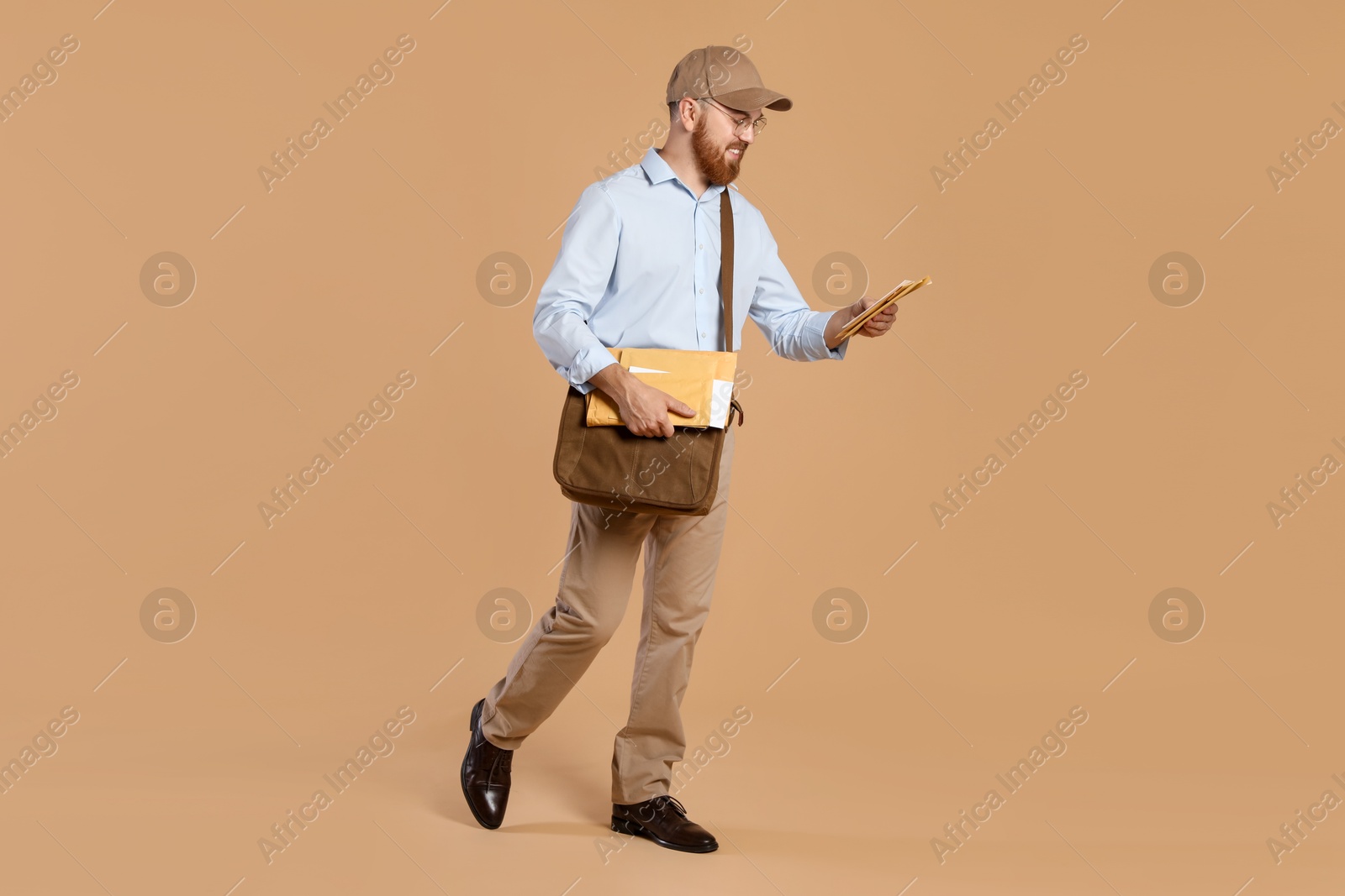 Photo of Happy young postman with leather bag delivering letters on brown background