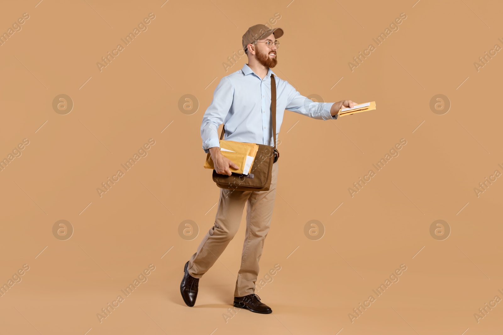 Photo of Happy young postman with leather bag delivering letters on brown background