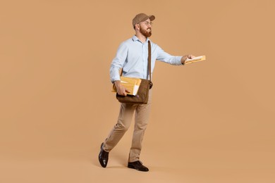 Happy young postman with leather bag delivering letters on brown background