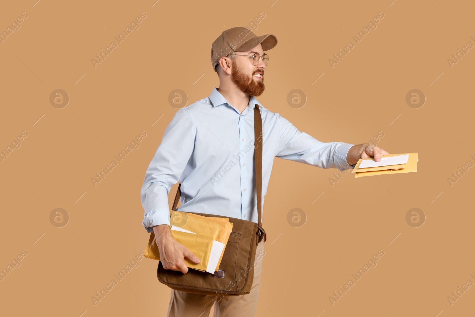 Photo of Happy young postman with leather bag delivering letters on brown background