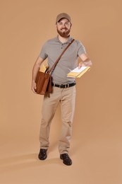 Photo of Happy young postman with leather bag delivering letters on brown background