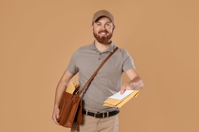 Photo of Happy young postman with leather bag delivering letters on brown background