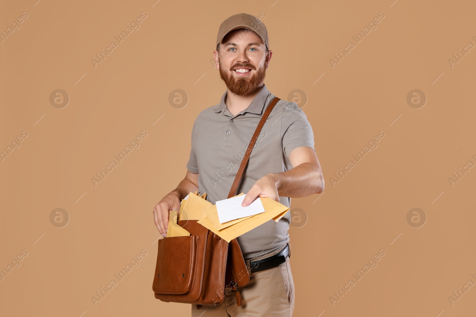 Photo of Happy young postman with leather bag delivering letters on brown background