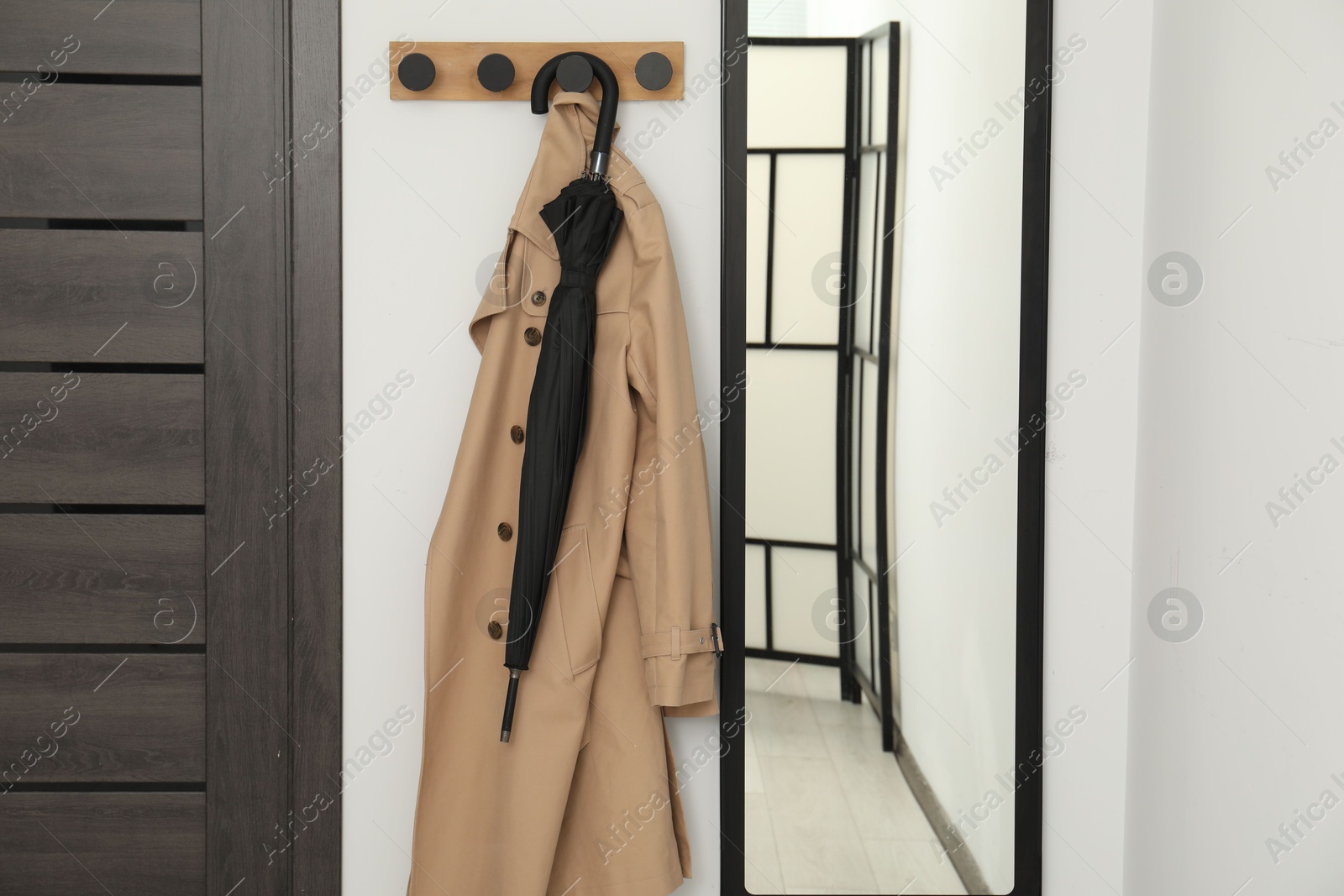 Photo of Black umbrella, coat, rack and mirror in hallway