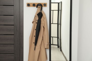 Photo of Black umbrella, coat, rack and mirror in hallway