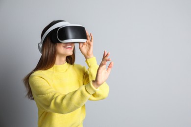 Photo of Smiling woman using virtual reality headset on light grey background. Space for text