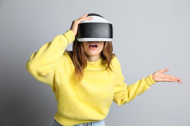Photo of Surprised woman using virtual reality headset on light grey background