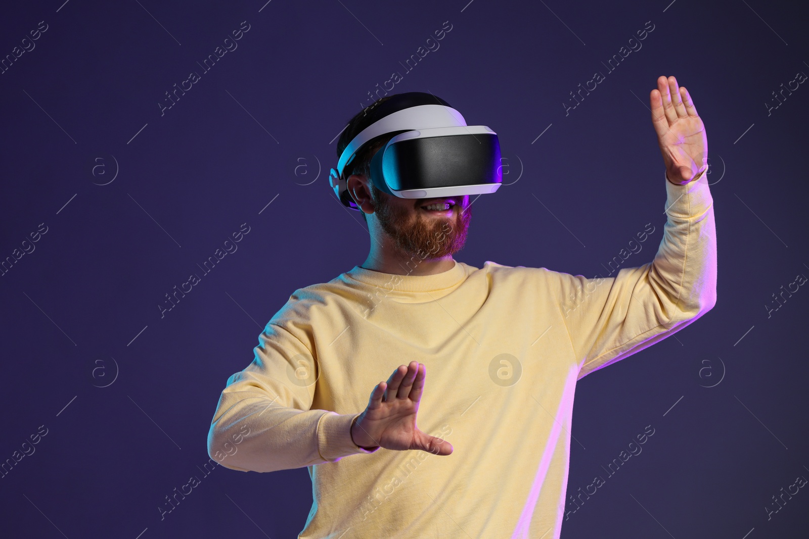 Photo of Smiling man using virtual reality headset on dark purple background