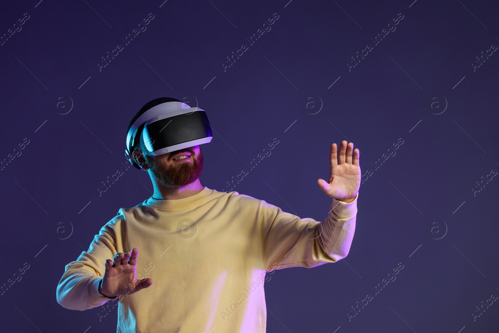 Photo of Man using virtual reality headset on dark purple background. Space for text