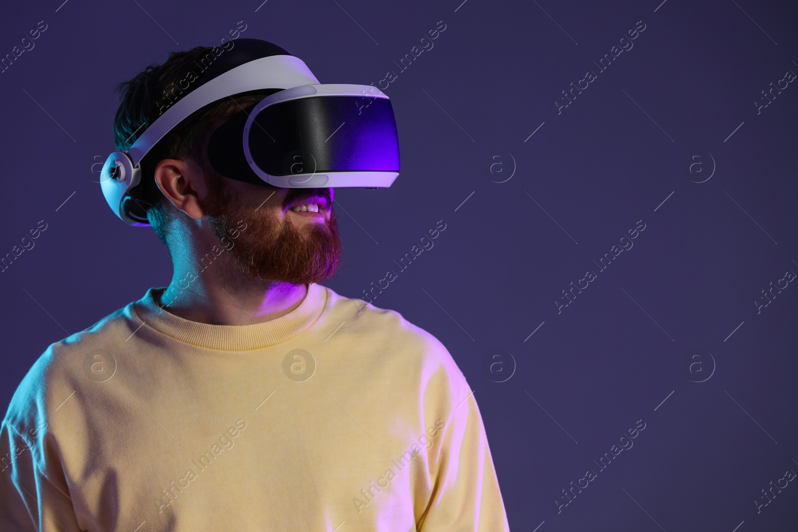 Photo of Man using virtual reality headset on dark purple background. Space for text