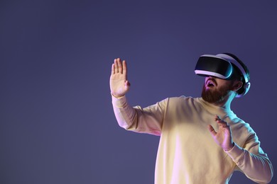 Photo of Emotional man using virtual reality headset on dark purple background. Space for text