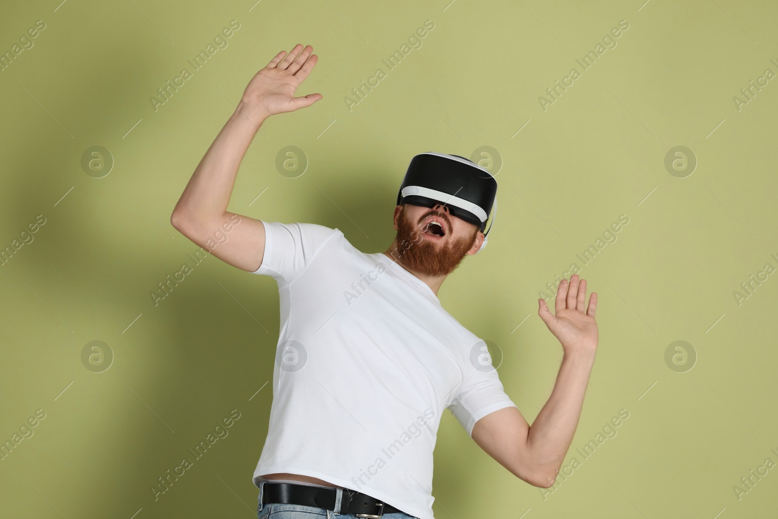 Photo of Emotional man using virtual reality headset on pale green background