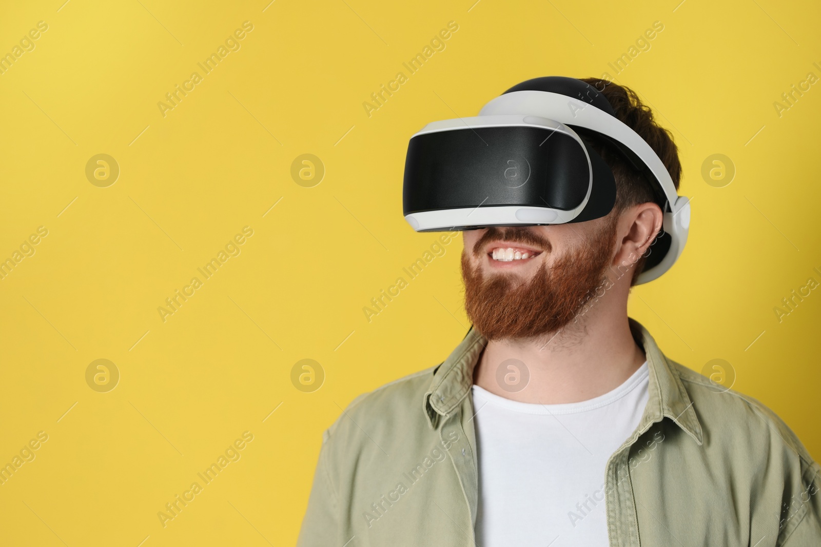 Photo of Smiling man using virtual reality headset on pale yellow background. Space for text