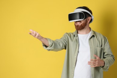 Photo of Smiling man using virtual reality headset on pale yellow background. Space for text