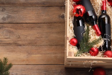 Photo of Wooden crate with bottles of wine, fir twigs and red Christmas balls on table, top view. Space for text