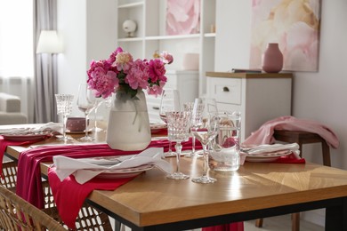 Photo of Pink peonies on table with beautiful setting and rattan chairs in dining room