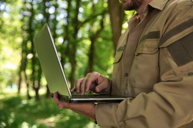 Photo of Forester with laptop examining plants in forest, closeup