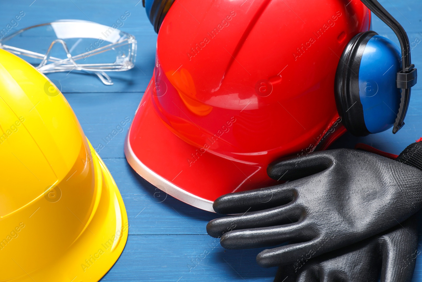 Photo of Hard hats, protective gloves, earmuffs and goggles on blue wooden background, closeup