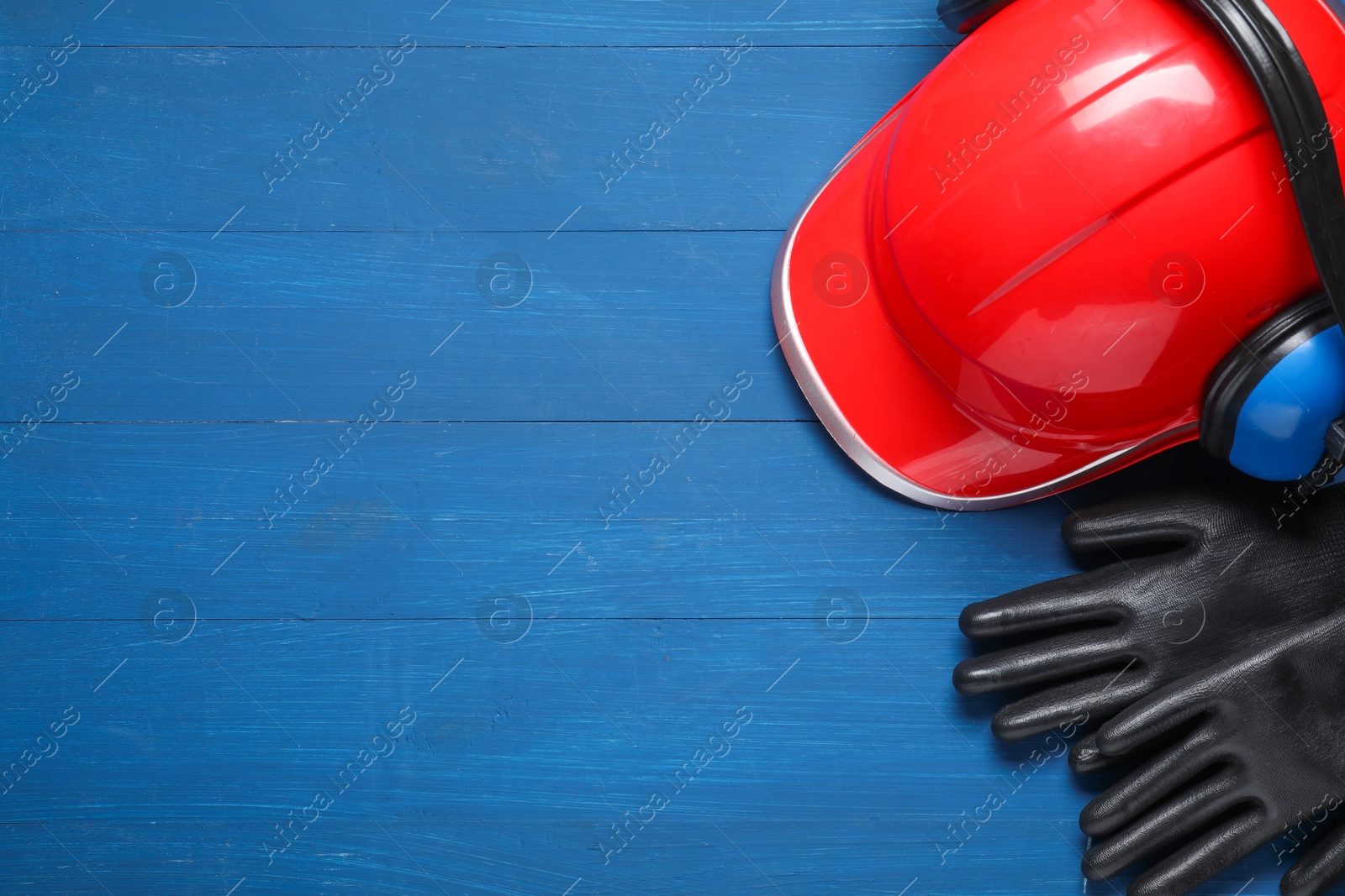 Photo of Hard hat, protective gloves and earmuffs on blue wooden background, flat lay. Space for text