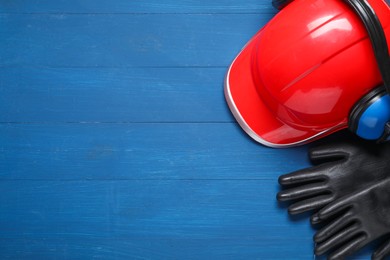 Photo of Hard hat, protective gloves and earmuffs on blue wooden background, flat lay. Space for text