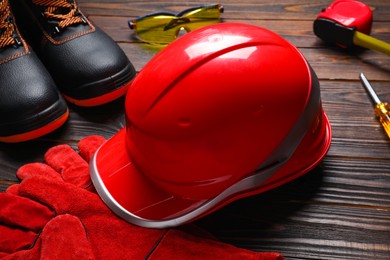 Hard hat, pair of working boots and protective gloves on wooden background, closeup