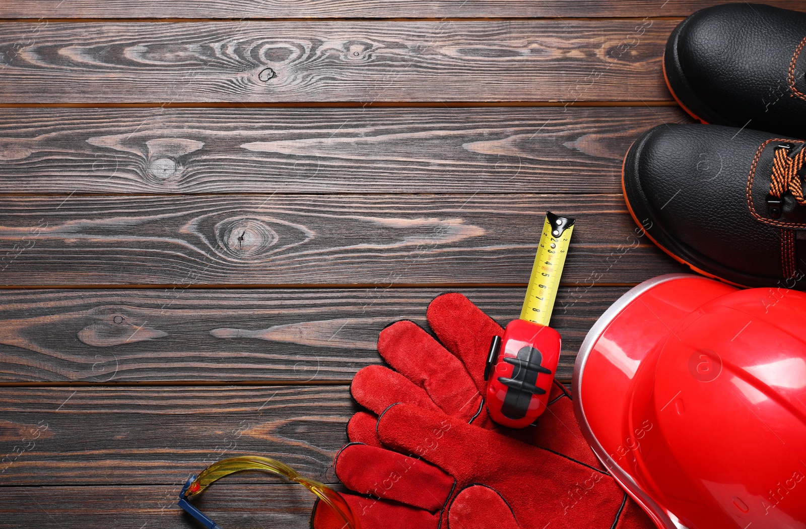 Photo of Pair of working boots, hard hat, protective gloves, goggles and tape measure on wooden background, flat lay. Space for text