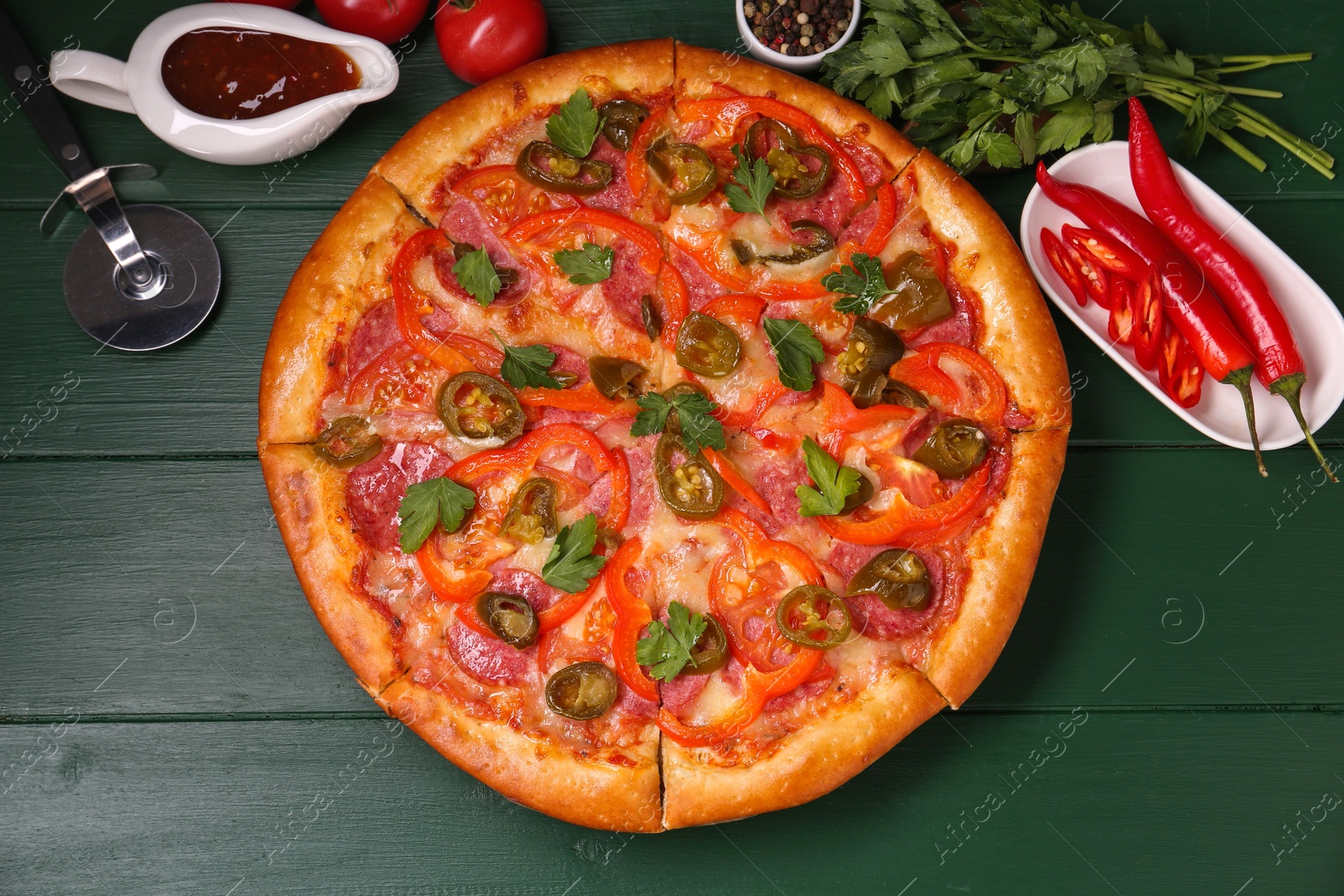 Photo of Delicious pizza Diablo, ingredients and cutter on green wooden table, flat lay