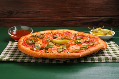 Photo of Delicious pizza Diablo, sauce and pickled peppers on green wooden table