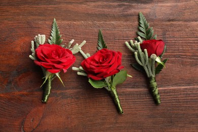 Many stylish red boutonnieres on wooden table, flat lay