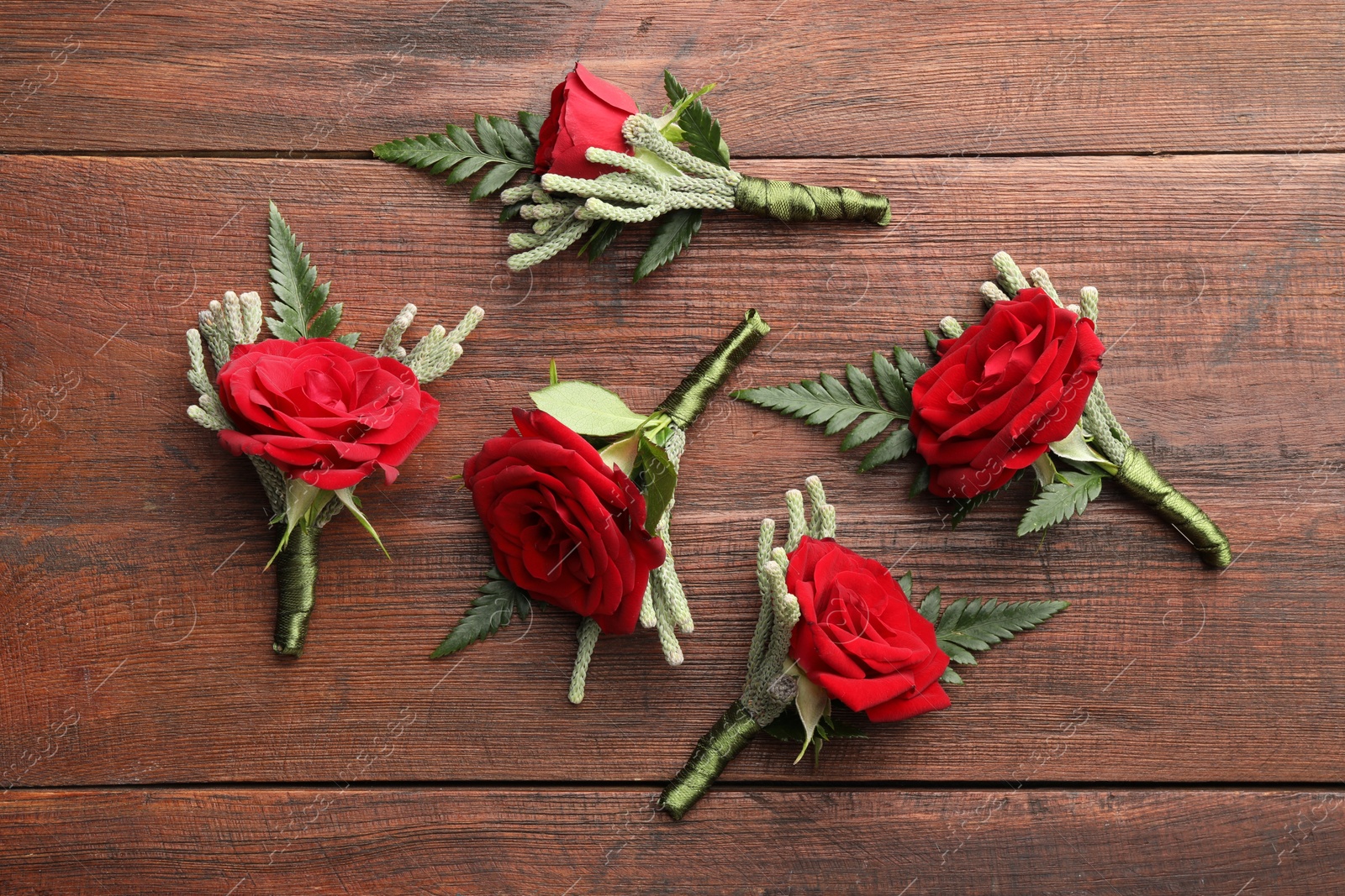 Photo of Many stylish red boutonnieres on wooden table, flat lay