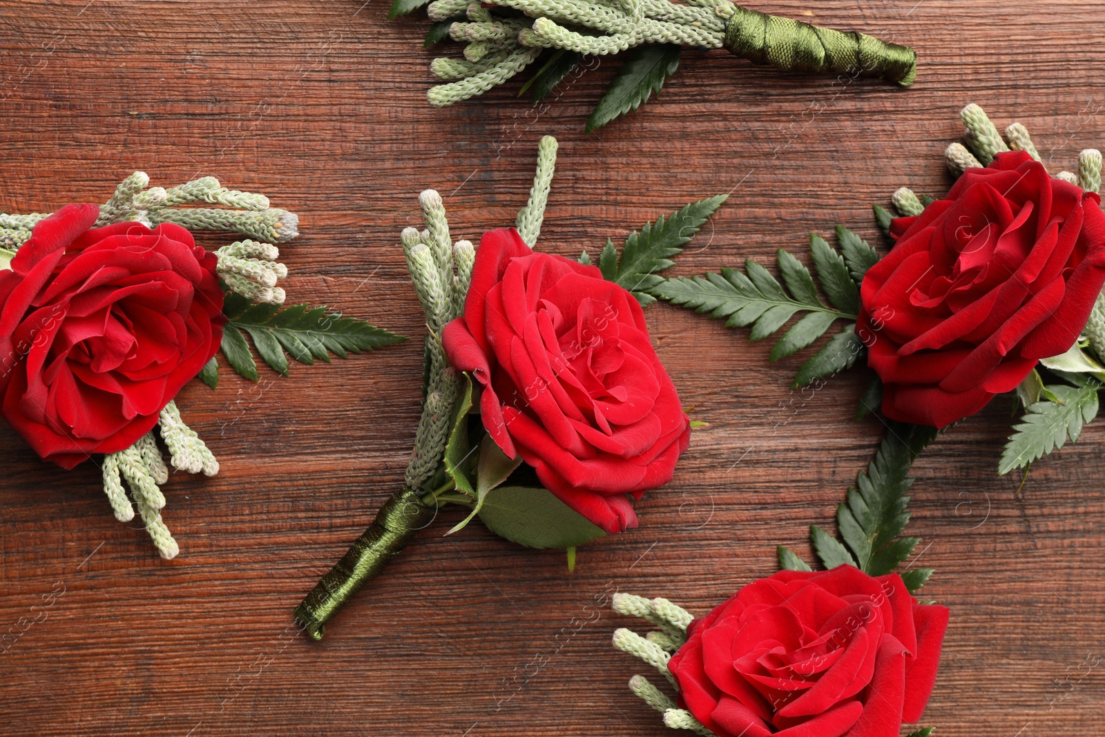 Photo of Many stylish red boutonnieres on wooden table, flat lay