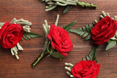 Many stylish red boutonnieres on wooden table, flat lay