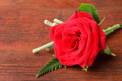 One stylish red boutonniere on wooden table, closeup. Space for text