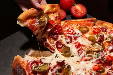 Woman taking piece of delicious pizza Diablo on black background, closeup