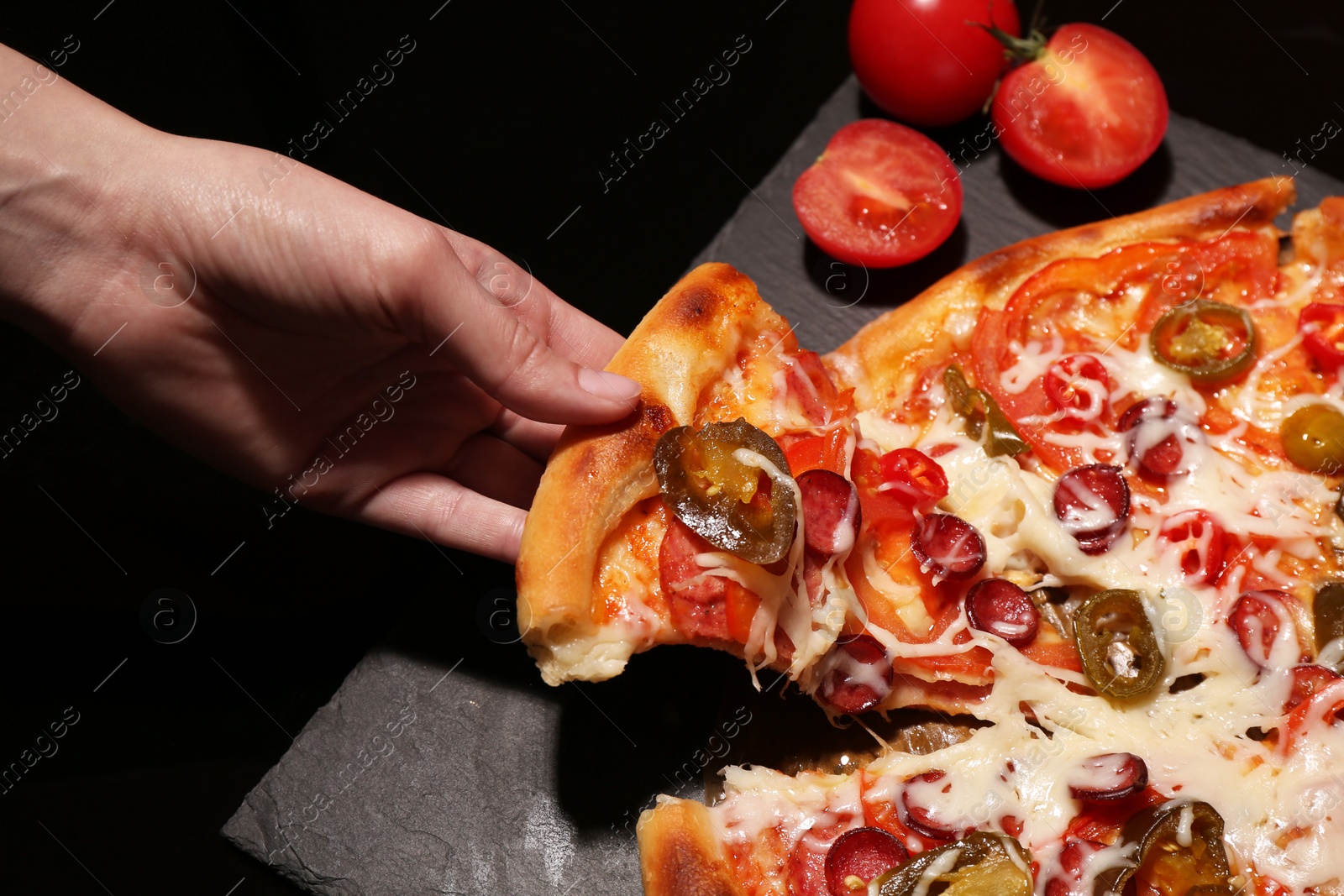 Photo of Woman taking piece of delicious pizza Diablo on black background, closeup