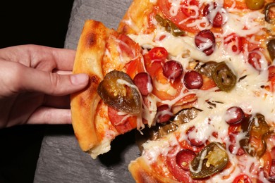 Photo of Woman taking piece of delicious pizza Diablo on black background, above view