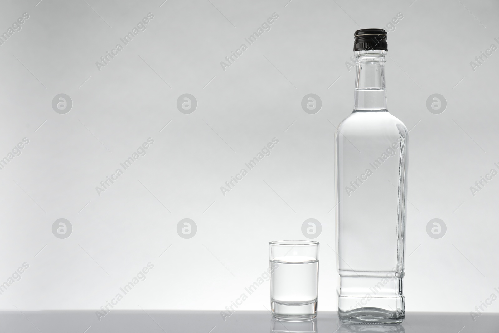 Photo of Bottle and glass with vodka on white table against light background, space for text