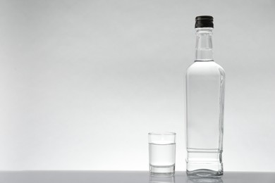 Bottle and glass with vodka on white table against light background, space for text