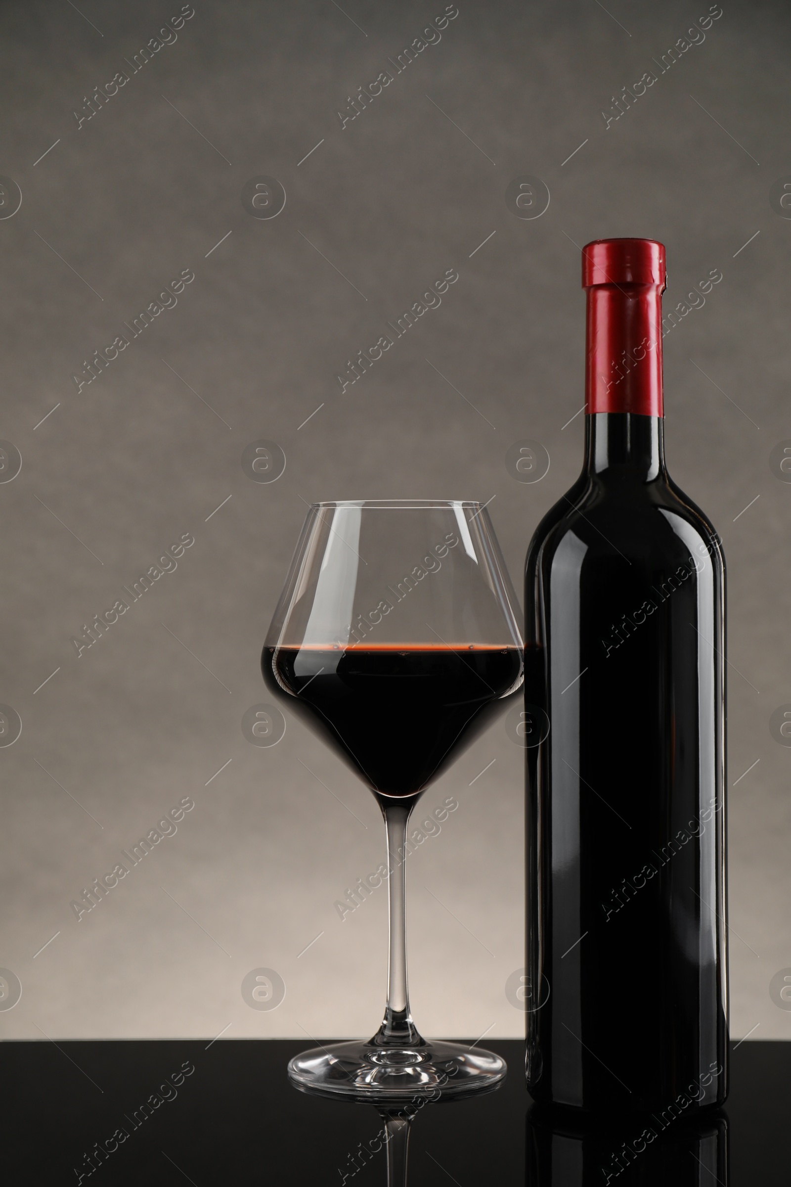 Photo of Bottle and glass with red wine on table against gray background