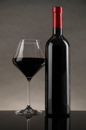 Photo of Bottle and glass with red wine on table against gray background