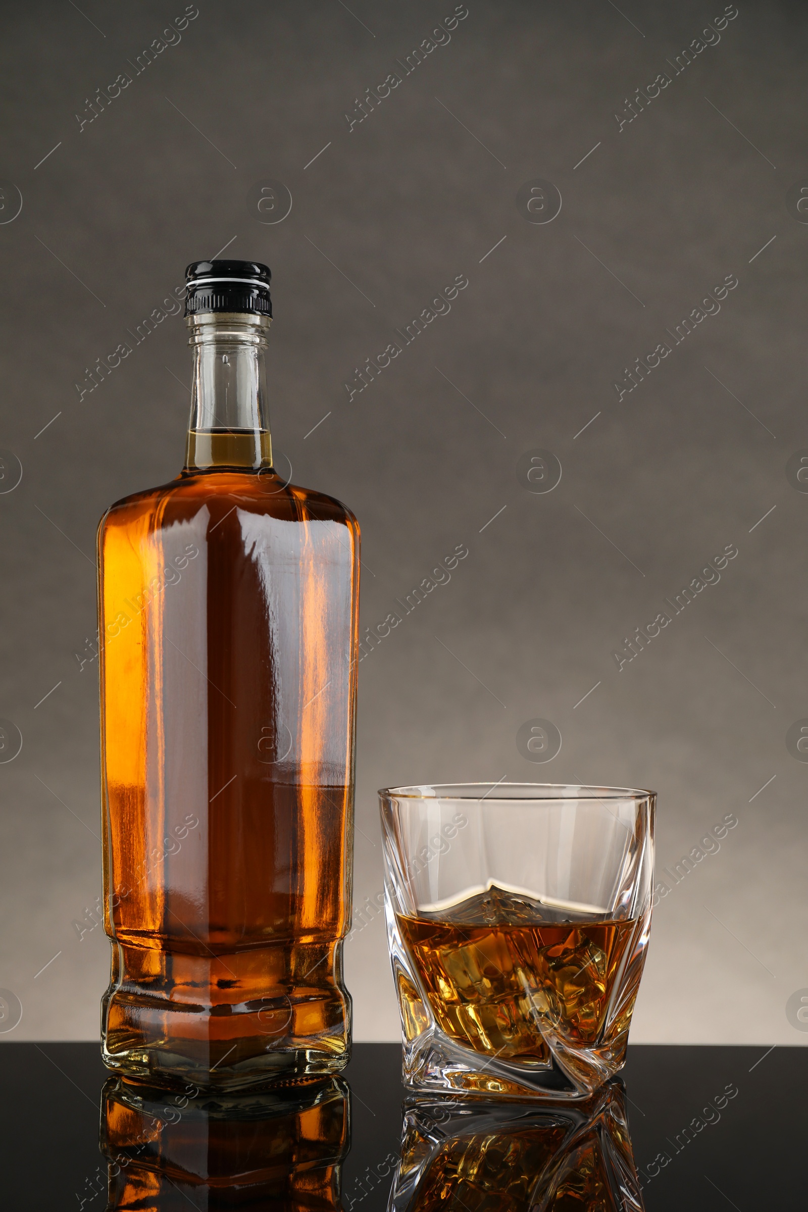 Photo of Bottle and glass with whiskey on table against gray background