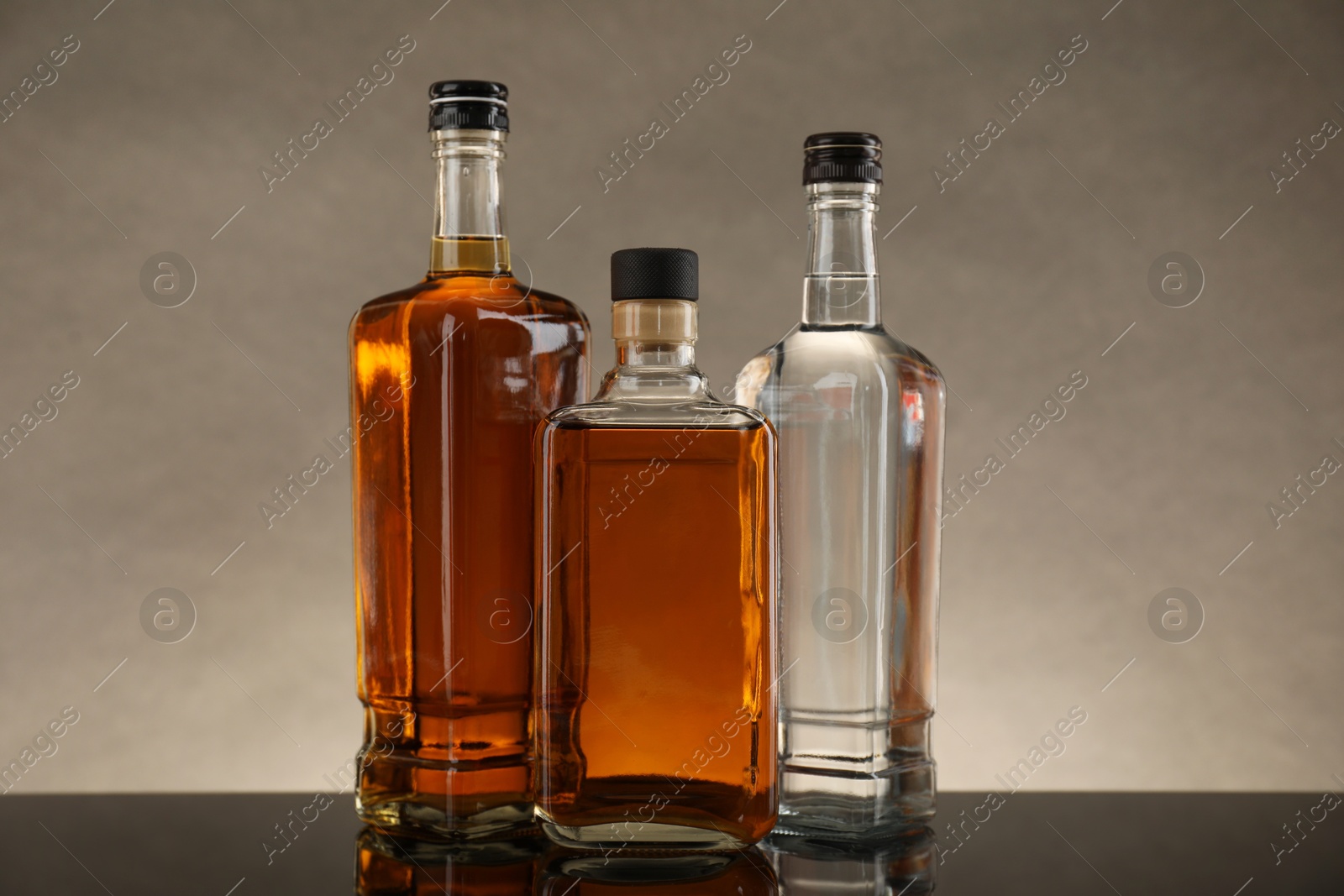 Photo of Bottles of different alcoholic drinks on table against gray background