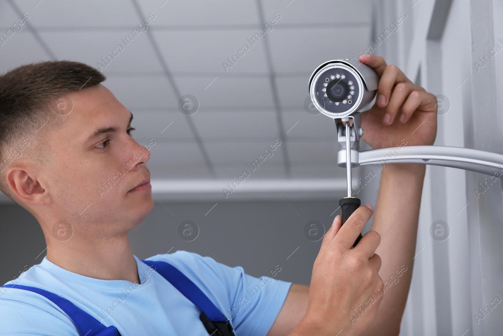 Photo of Technician with screwdriver installing CCTV camera on wall indoors